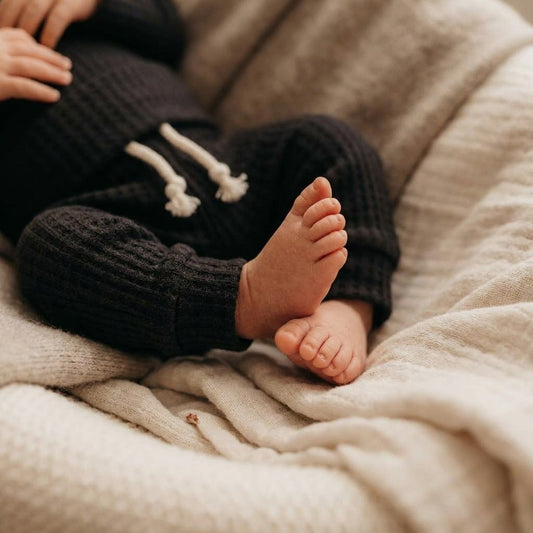 Close-up of a baby's bare feet and legs wearing black waffle knit pants with white drawstrings
