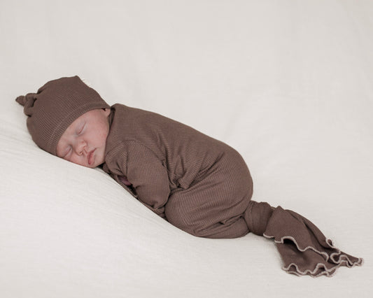 a sleeping newborn baby wearing a soft brown color knotted gown with matching hat