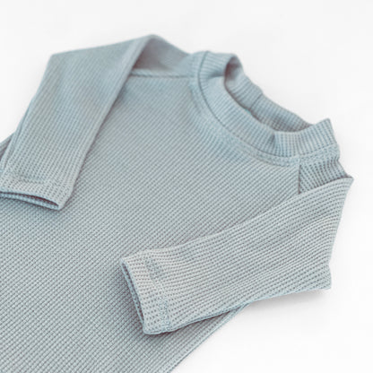 A close-up of a light blue thermal knit long-sleeve top with a crew neck