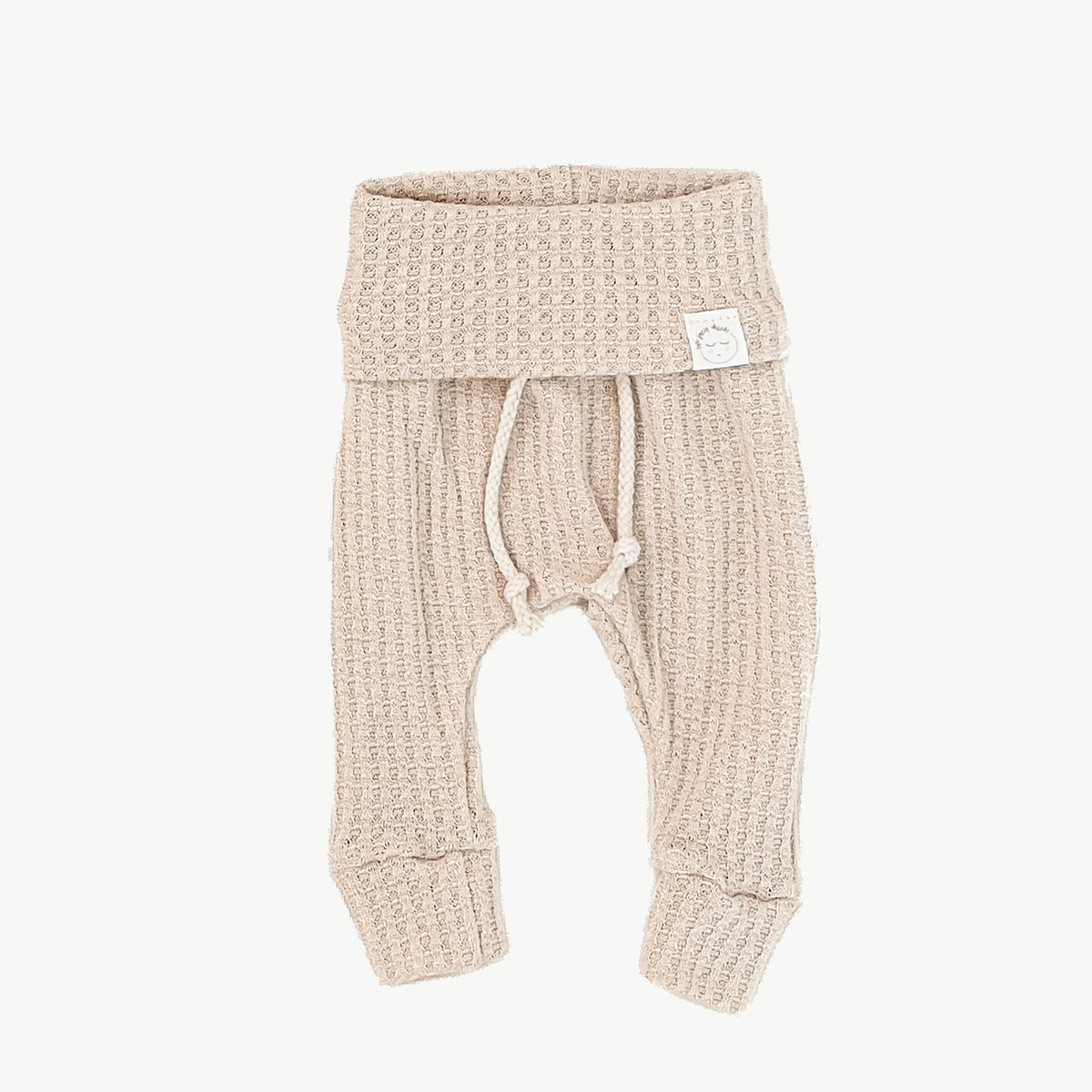 A pair of beige waffle-knit baby pants with a drawstring waist and ankle cuffs