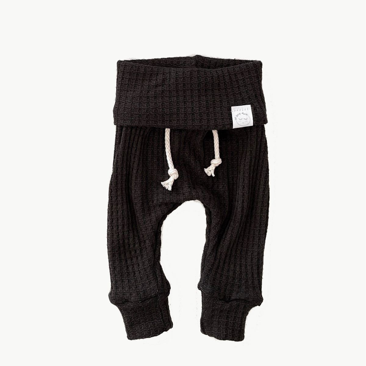 A pair of black waffle-knit baby pants with a drawstring waist and ankle cuffs
