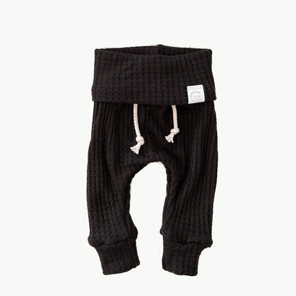 A pair of black waffle-knit baby pants with a drawstring waist and ankle cuffs