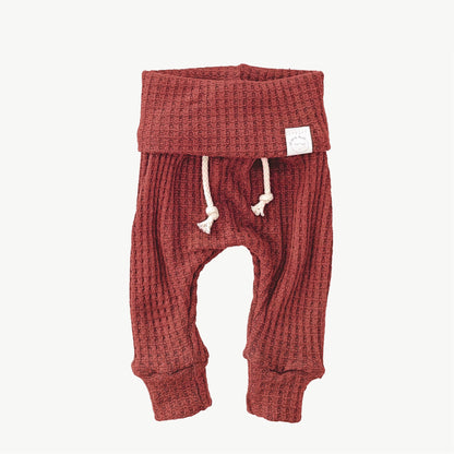 A pair of brick red waffle-knit baby pants with a drawstring waist and ankle cuffs