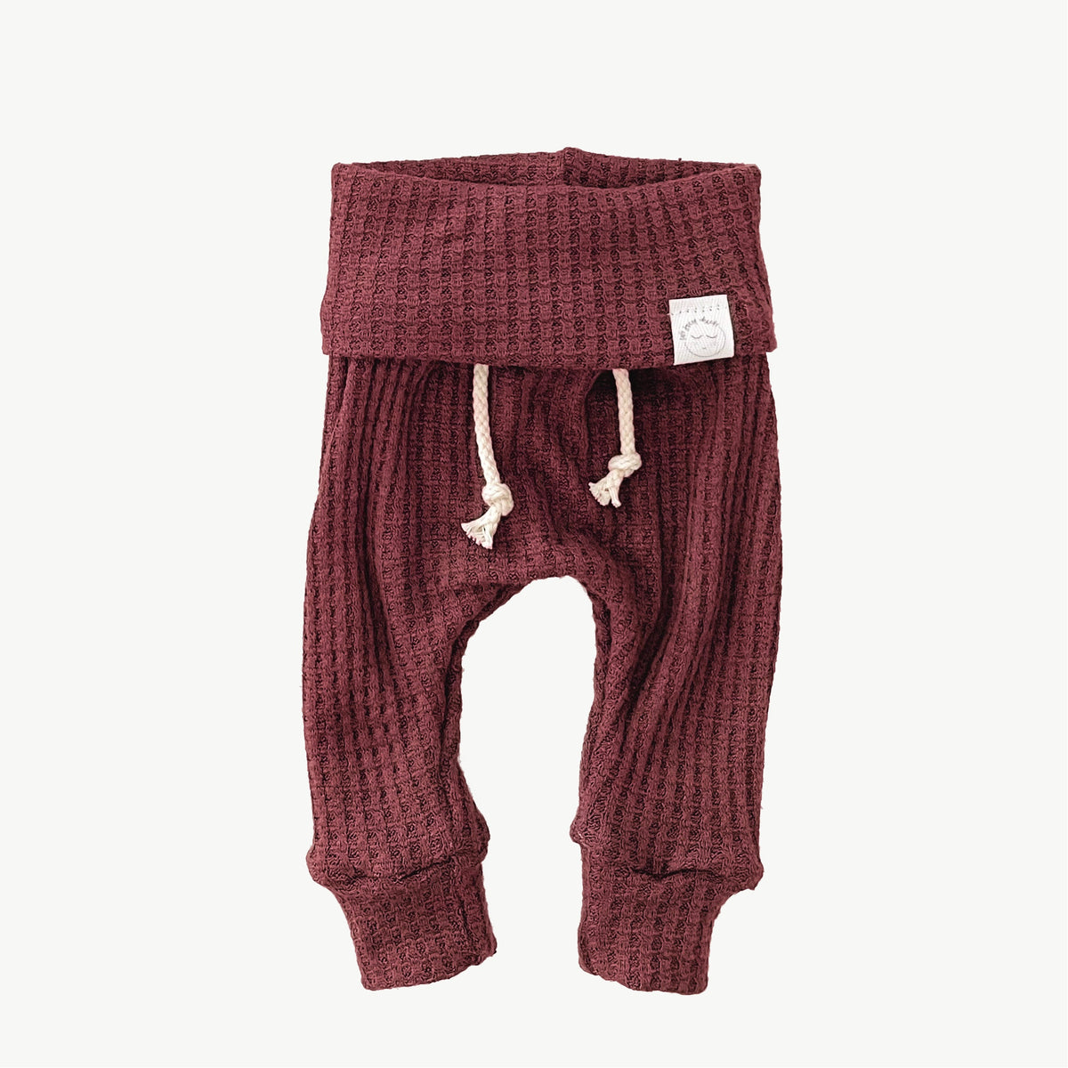 A pair of cranberry waffle-knit baby pants with a drawstring waist and ankle cuffs