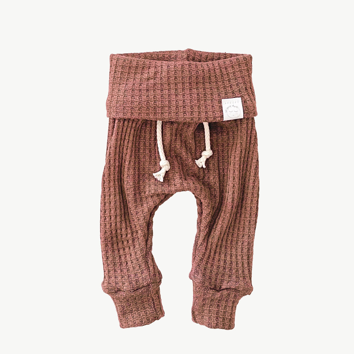 A pair of dusty rose waffle-knit baby pants with a drawstring waist and ankle cuffs