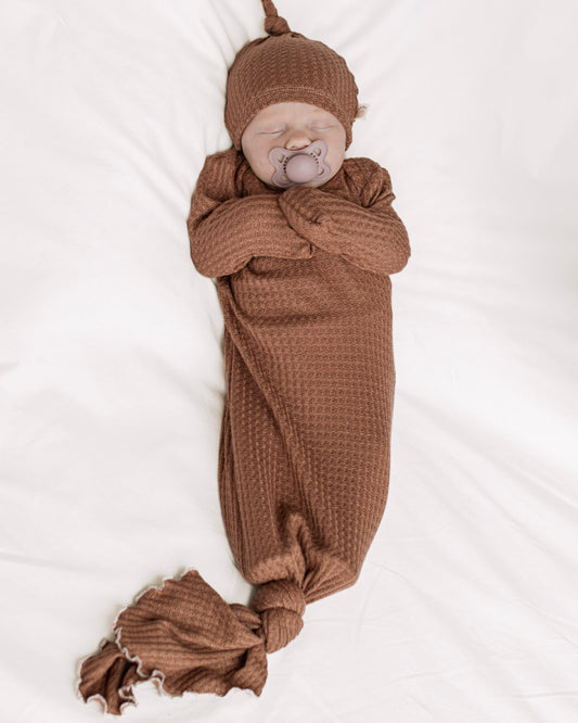 A newborn baby wrapped in a brown waffle-knit gown and matching knit hat