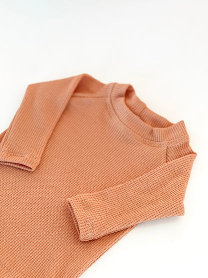 A close-up of a peach-colored ribbed knit long-sleeve top with a crew neck,
