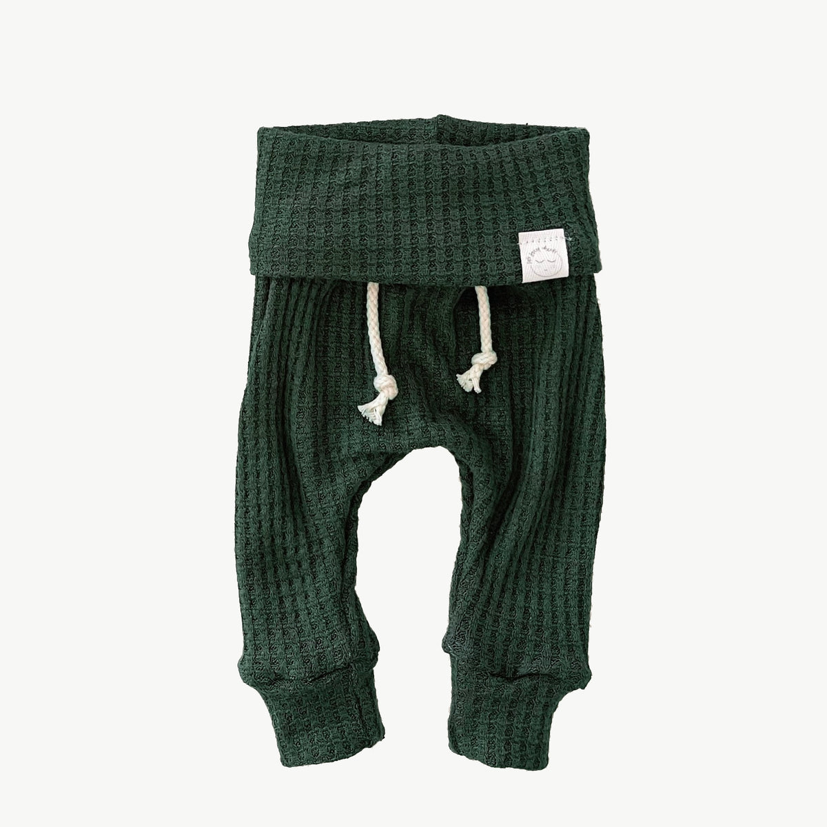 A pair of pine green waffle-knit baby pants with a drawstring waist and ankle cuffs