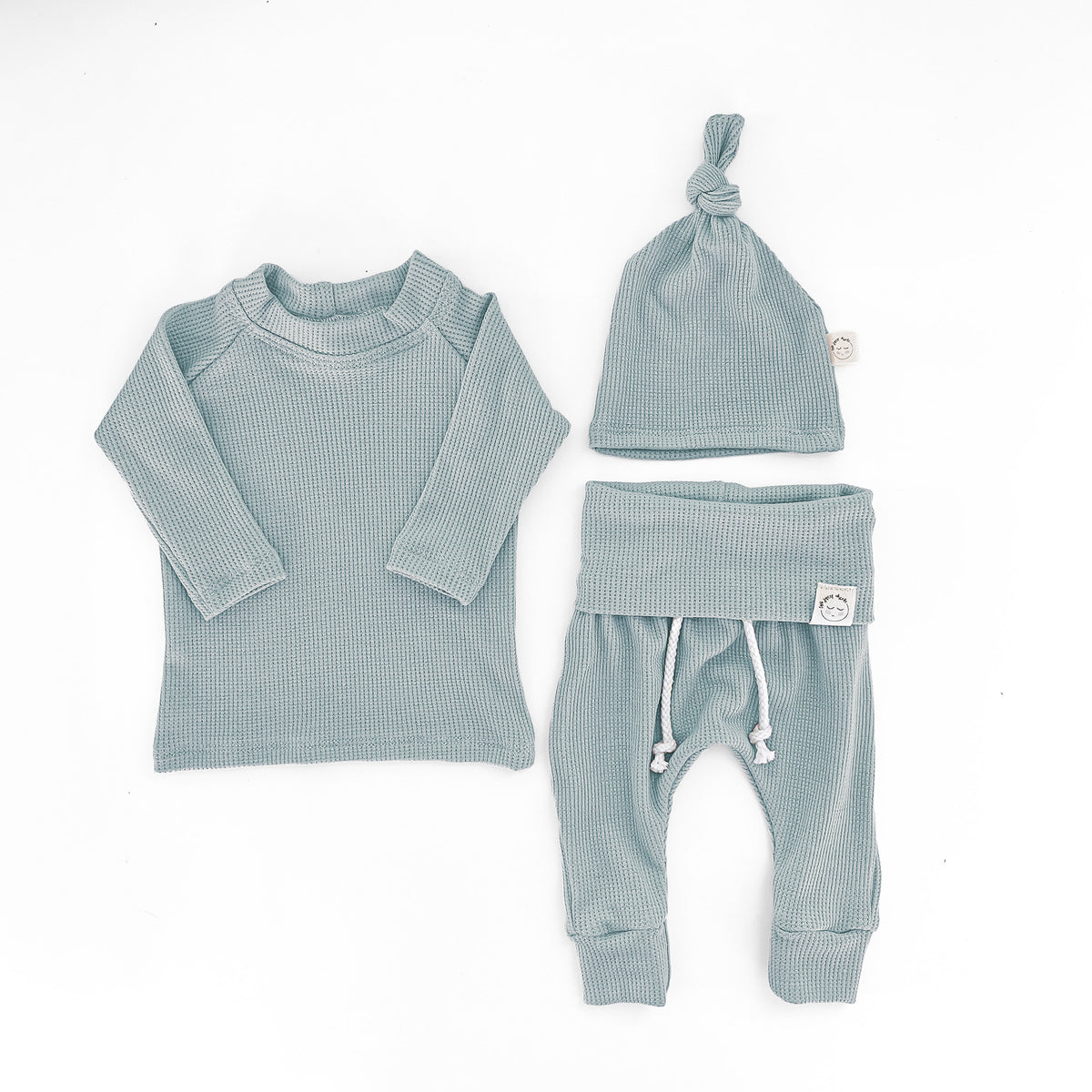 A three-piece baby clothing set in a mint blue color, including a long-sleeve ribbed top, matching pants with white drawstrings, and a knotted beanie hat