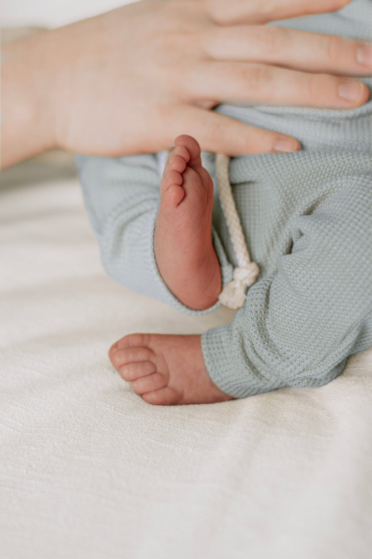 A close-up lifestyle shot of a baby wearing a light blue waffle-knit pants with a cream rope drawstring