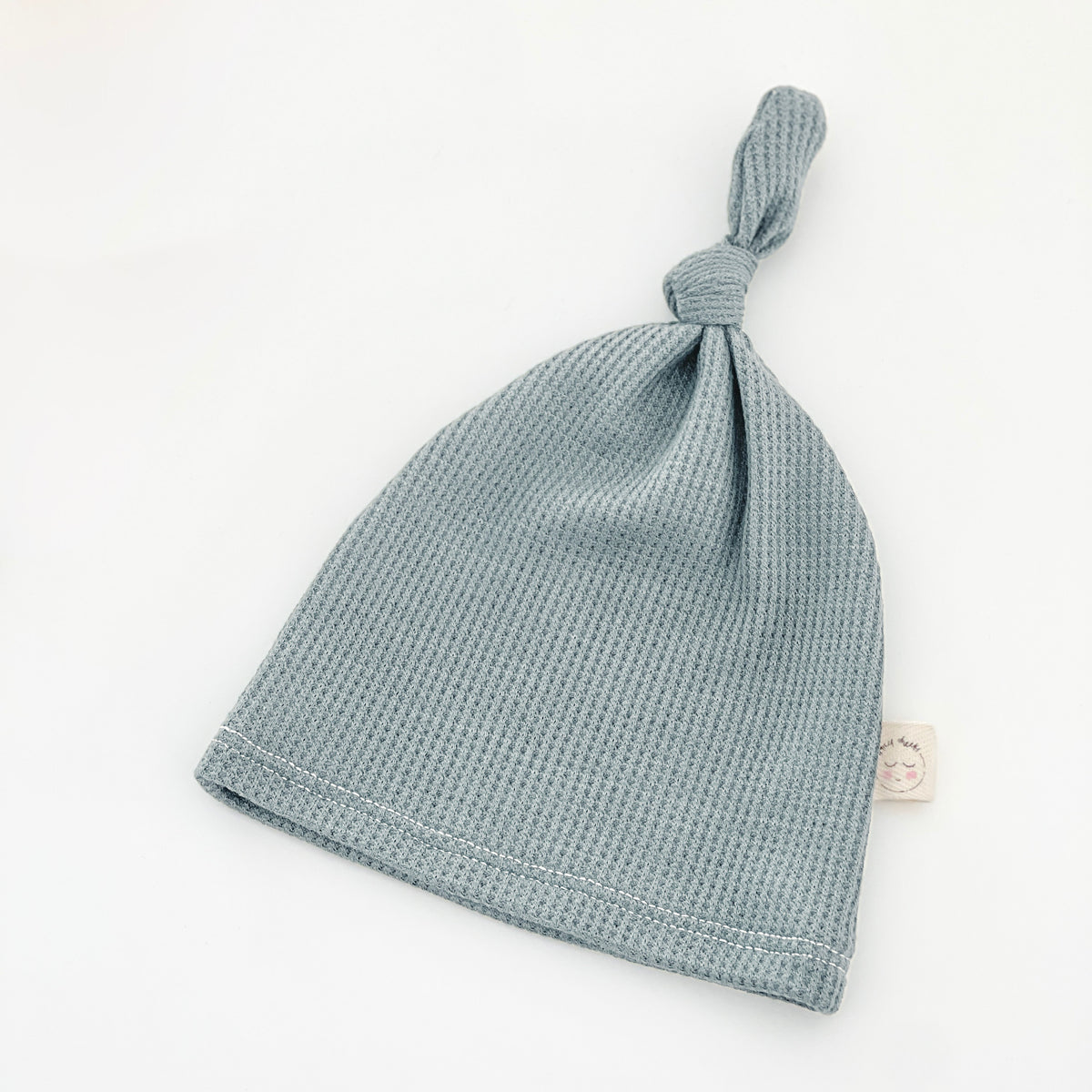 A dusty blue waffle-knit baby beanie hat with a knotted top
