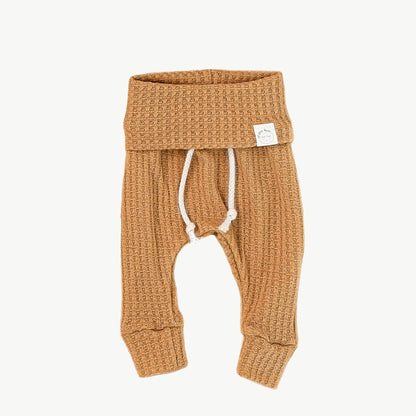 A pair of mustard waffle-knit baby pants with a drawstring waist and ankle cuffs