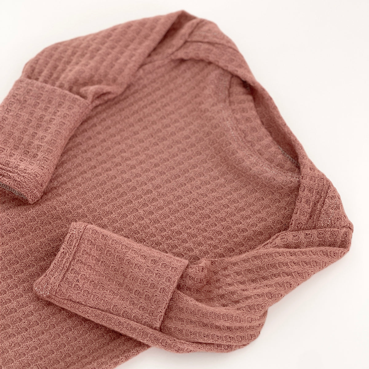 A close-up of a dusty rose waffle-knit long-sleeve gown, showing the textured fabric and folded cuffs