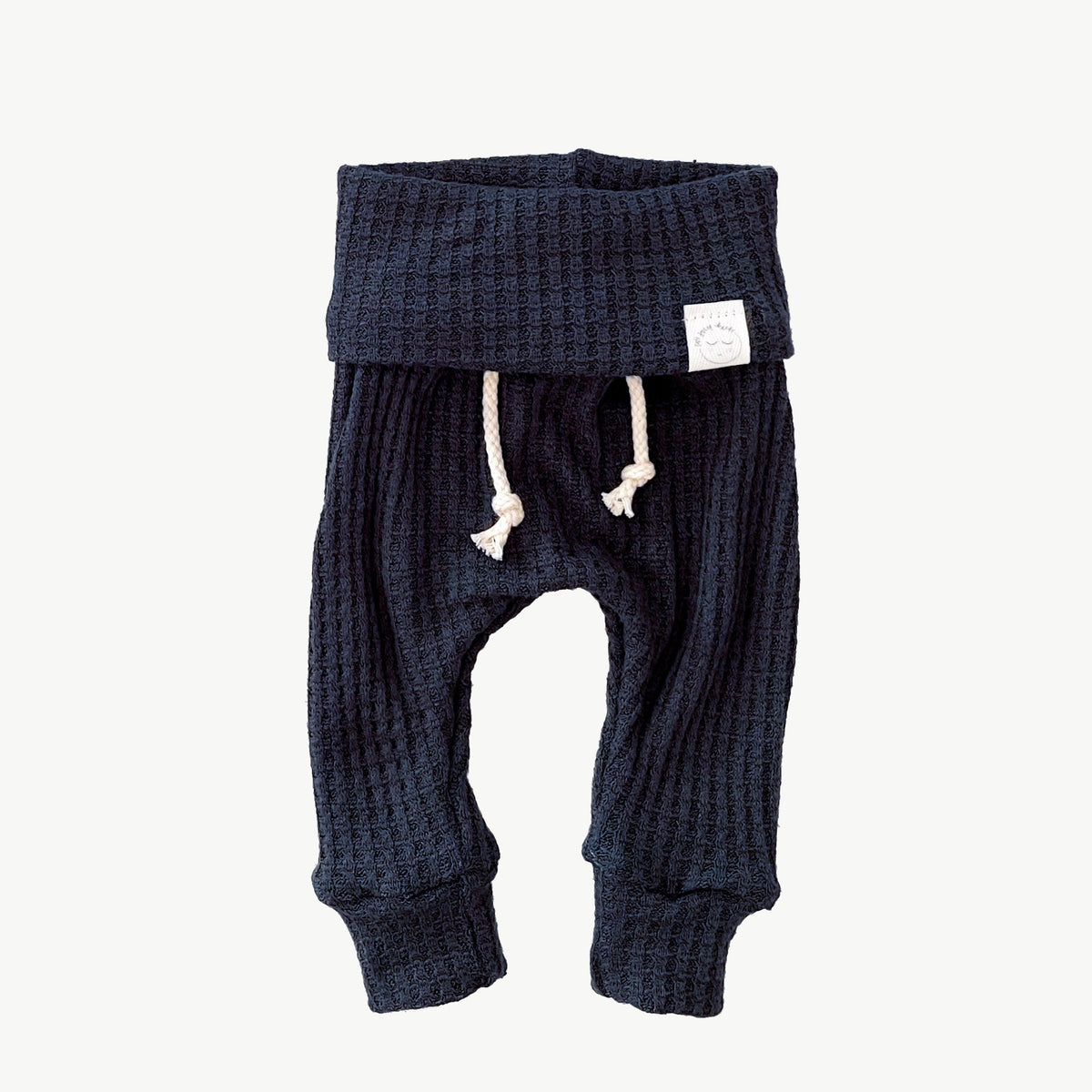 A pair of navy blue waffle-knit baby pants with a drawstring waist and ankle cuffs