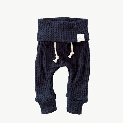 A pair of navy blue waffle-knit baby pants with a drawstring waist and ankle cuffs