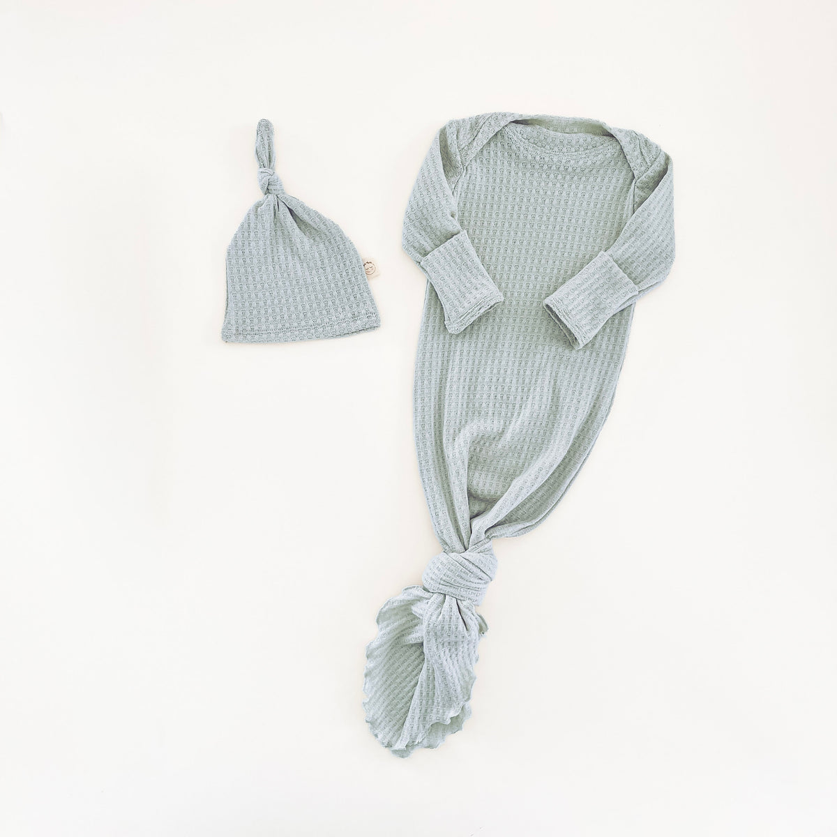 A baby knit set in a mint blue color, featuring a long-sleeve knotted gown and a matching knotted hat