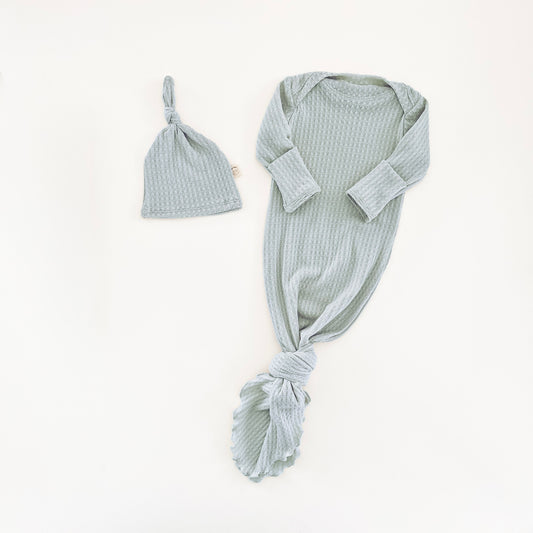 A baby knit set in a mint blue color, featuring a long-sleeve knotted gown and a matching knotted hat