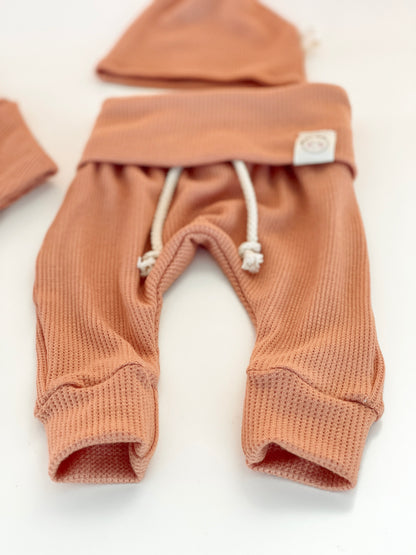A pair of terracotta waffle-knit baby pants with white drawstrings 