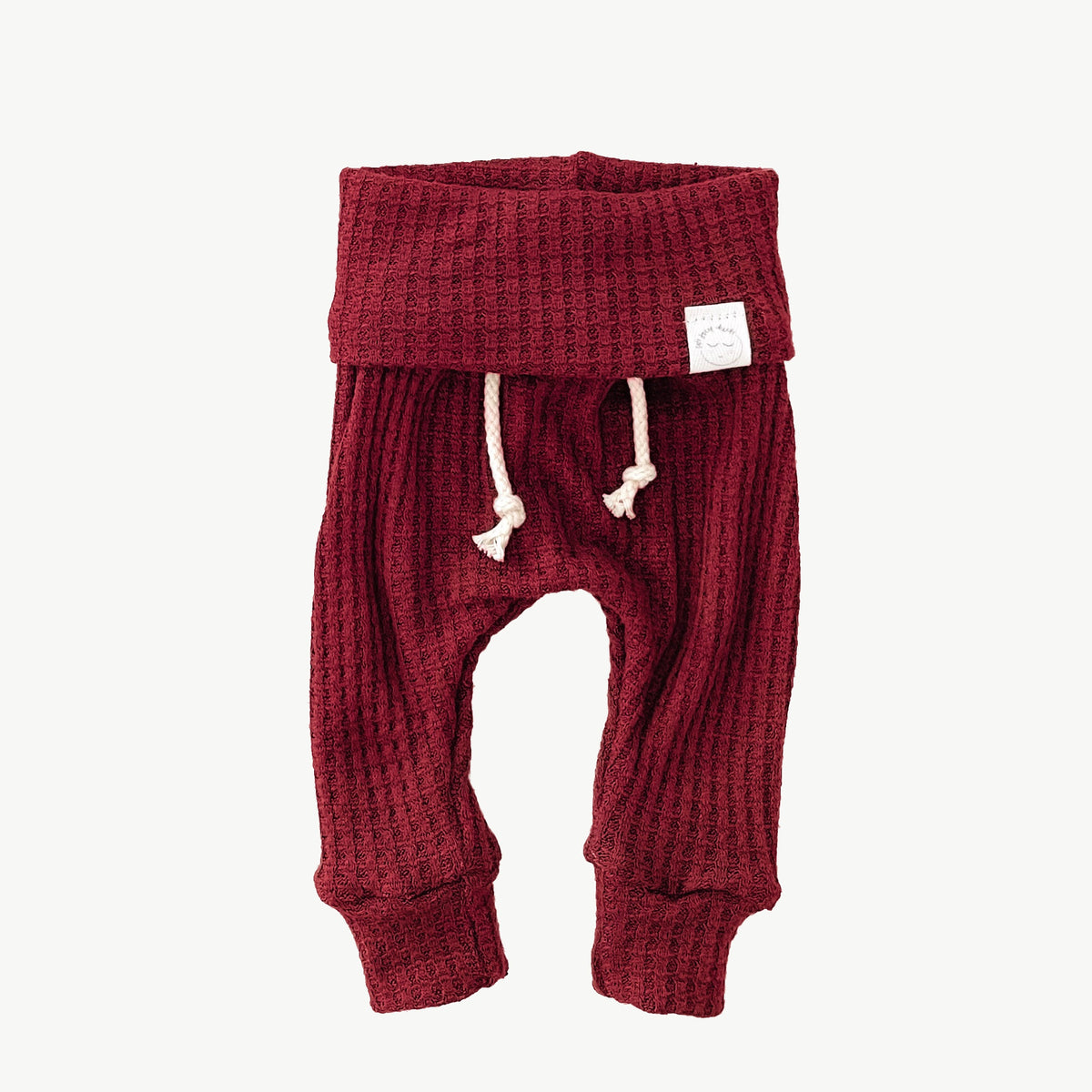 A pair of red waffle-knit baby pants with a drawstring waist and ankle cuffs