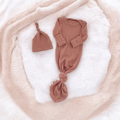 flat lay of a muted pink color baby gown with a matching knotted hat