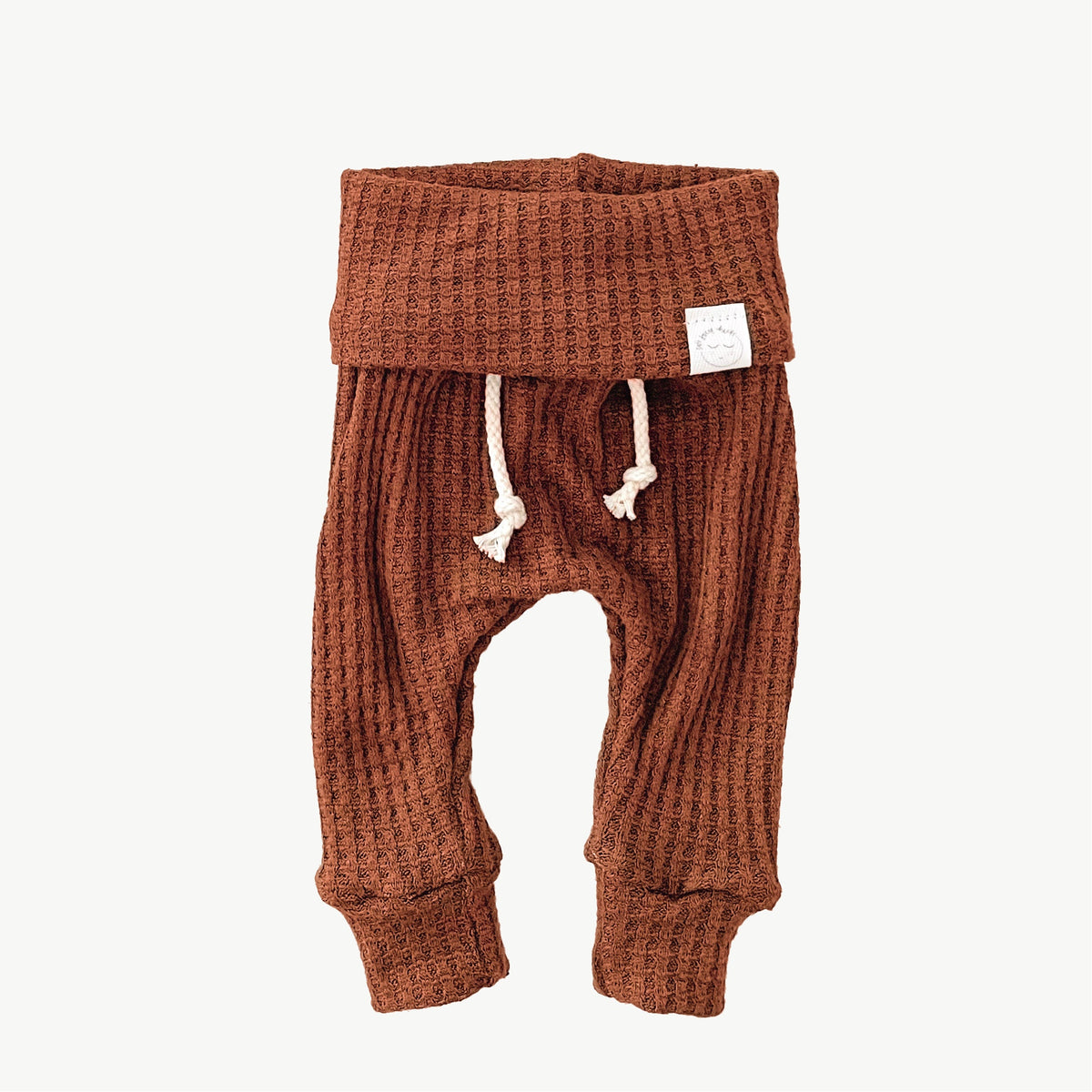 A pair of orange waffle-knit baby pants with a drawstring waist and ankle cuffs