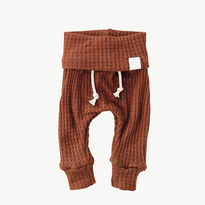 A pair of orange waffle-knit baby pants with a drawstring waist and ankle cuffs