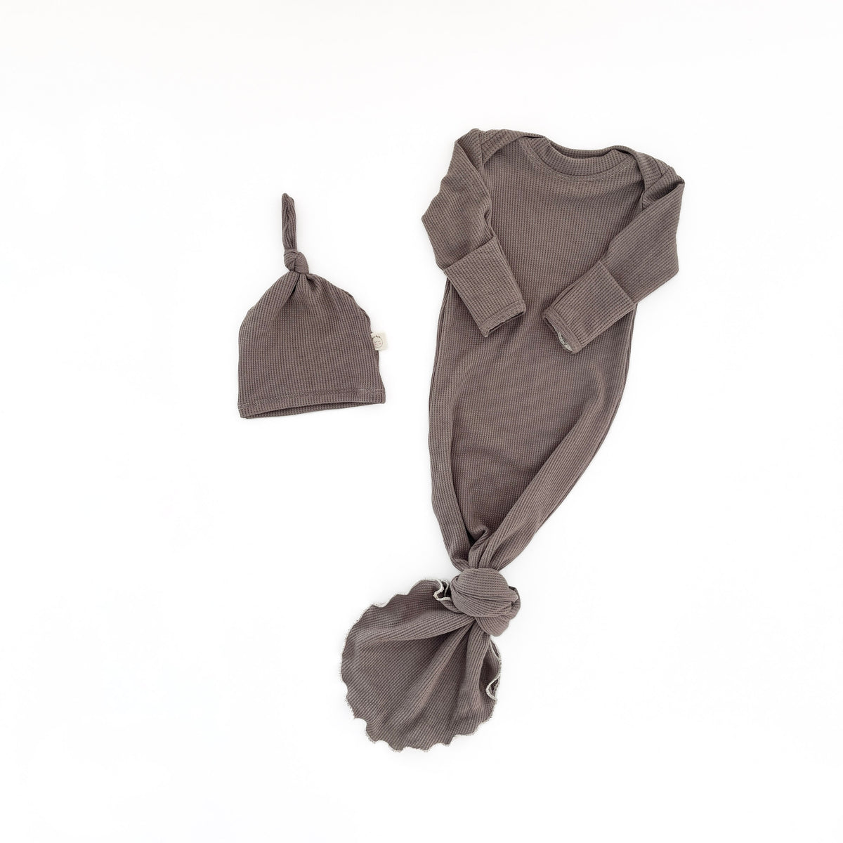 A baby knit set in a muted taupe-brown color, featuring a long-sleeve footless bodysuit with a knotted hem, a matching knotted beanie hat