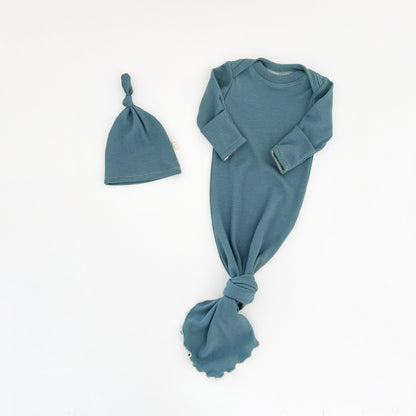 A baby clothing set featuring a long-sleeve knit gown and a matching knotted hat, both in a teal blue color