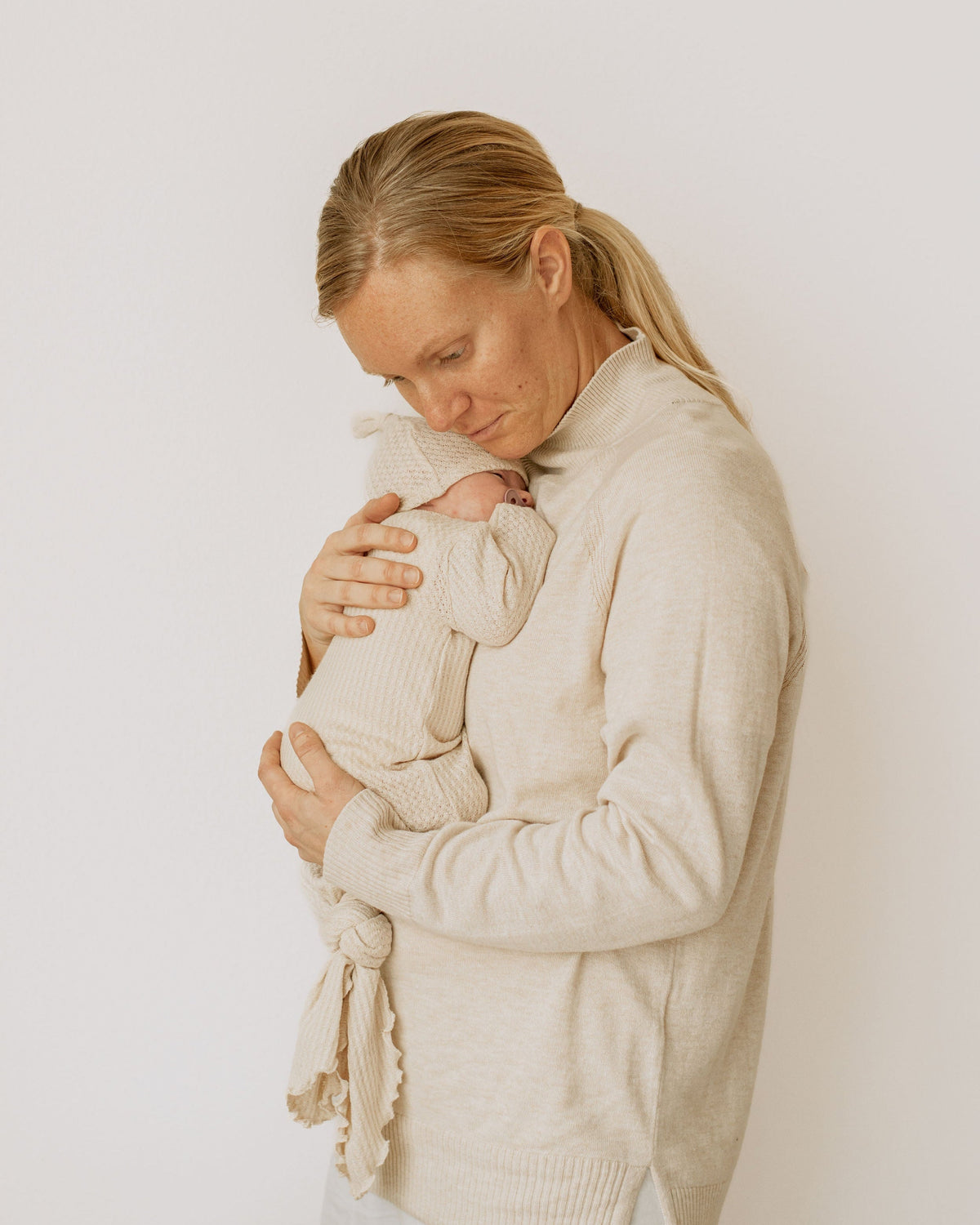 Two Sweet Cheeks newborn wearing a cream waffle knit knotted gown held by a woman in a matching sweater