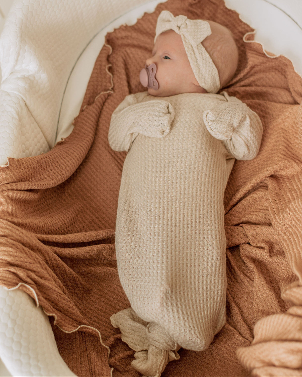 Newborn wearing a Two Sweet Cheeks oatmeal waffle knit knotted gown and matching headband while lying on a blanket.