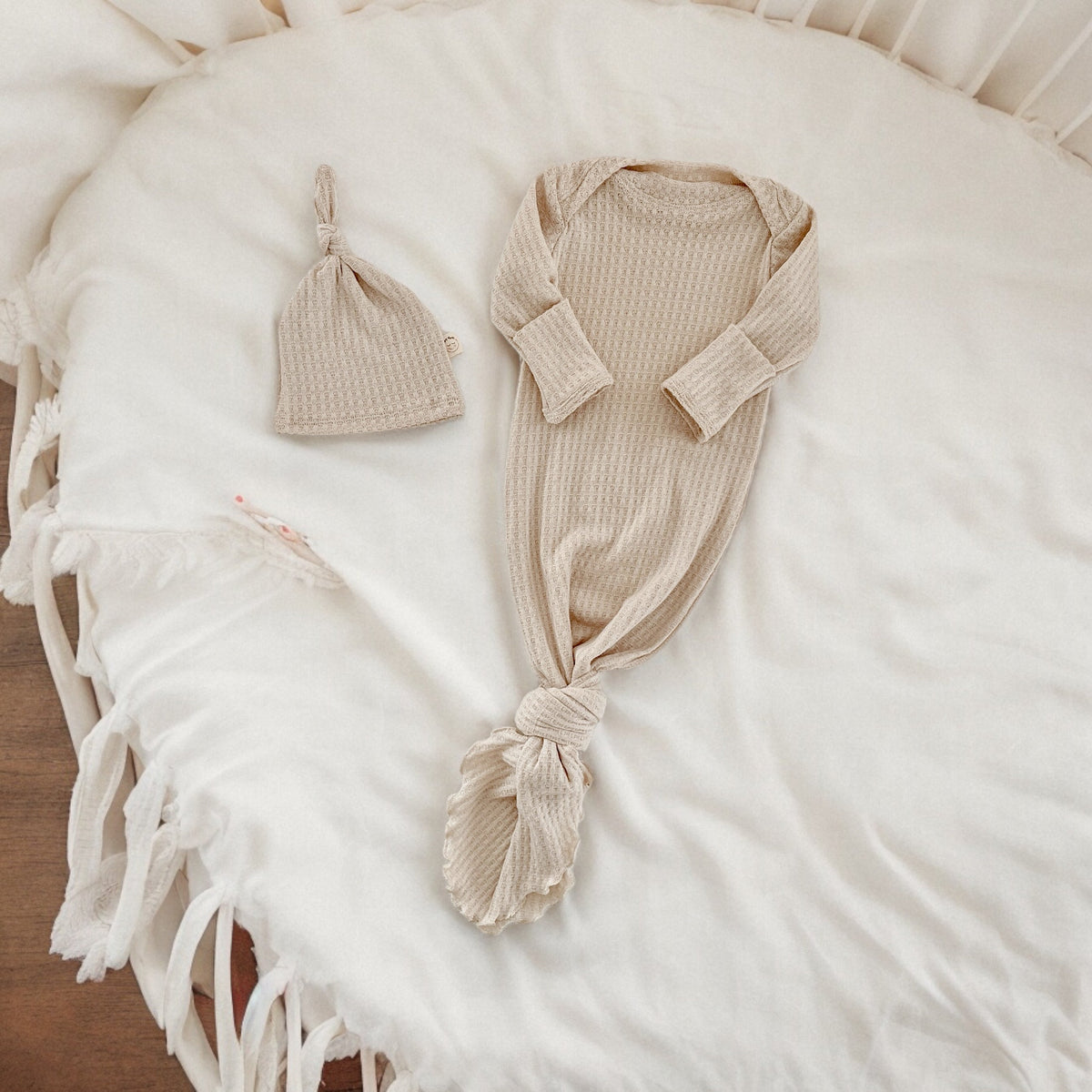 Two Sweet Cheeks oatmeal waffle knit newborn knotted gown and matching hat set on a white round baby bed