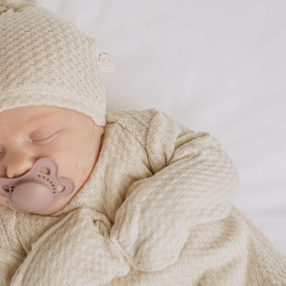 Two Sweet Cheeks oatmeal waffle knit newborn gown and matching hat on a sleeping baby with a neutral pacifier