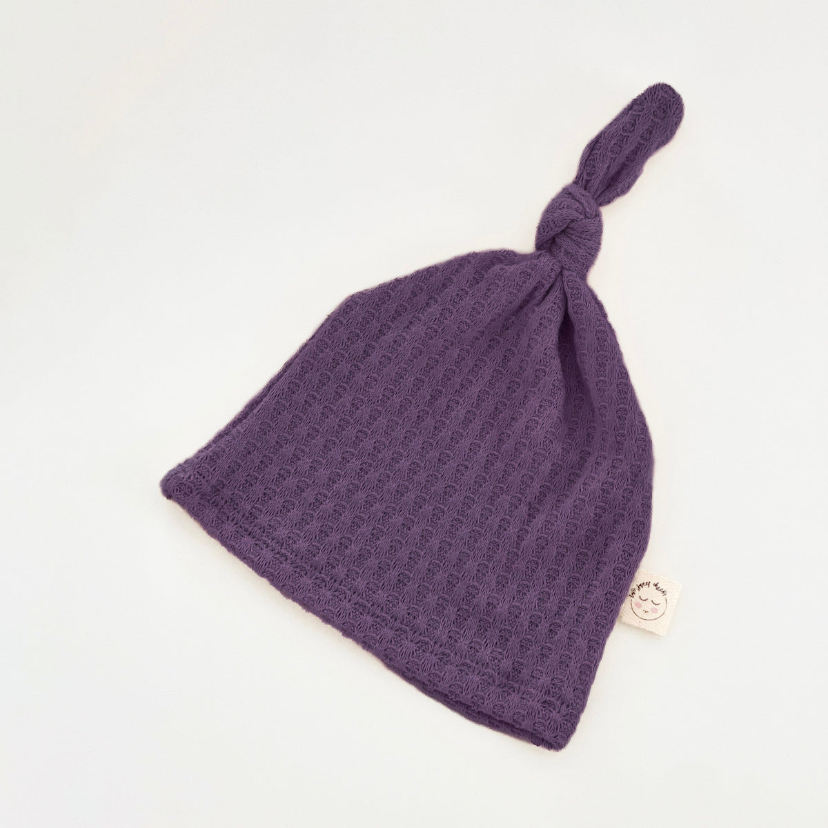 Two Sweet Cheeks plum purple waffle knit knotted baby hat with a soft, textured fabric and a side brand label.