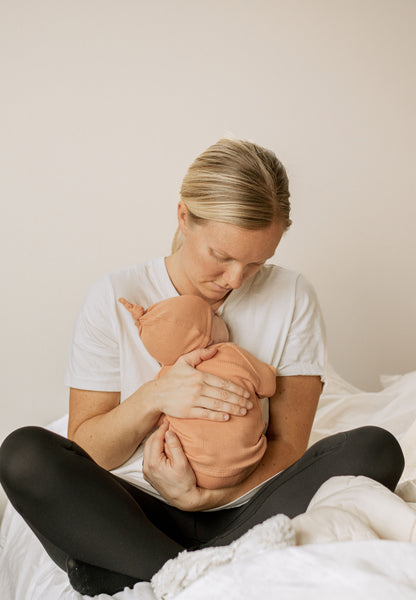 a mom holding a newborn baby in a peach outfit