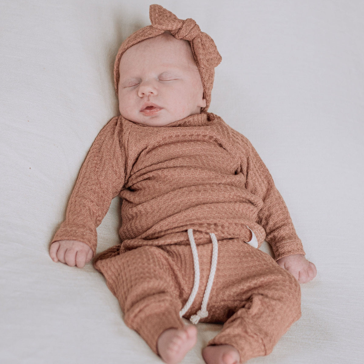 baby girl wearing dusty rose color shirt, pants, headband.