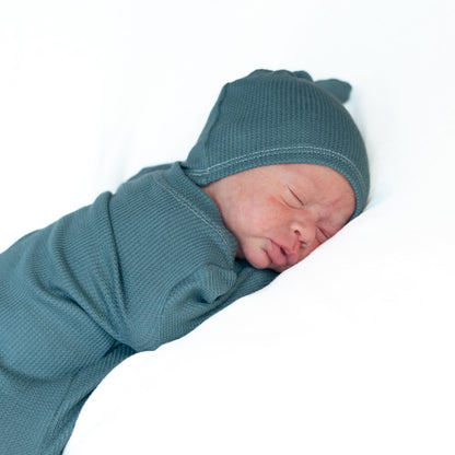 sleeping newborn boy wearing soft blue thermal gown and matching knot hat