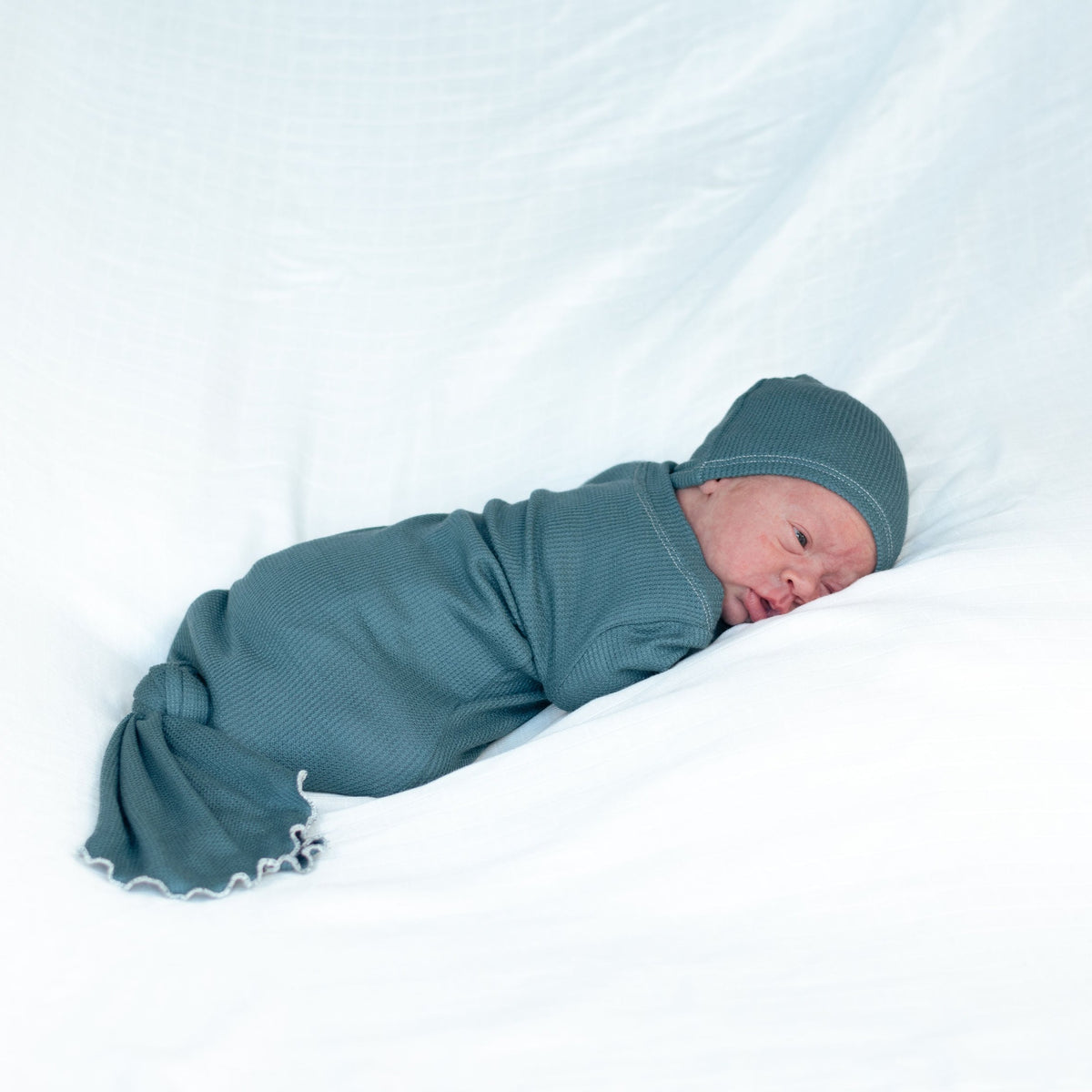 newborn baby boy wearing a teal thermal knotted gown and matching knot hat